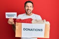 Young handsome man volunteer holding box and donations needed paper celebrating crazy and amazed for success with open eyes