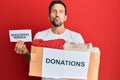 Young handsome man volunteer holding box and donations needed paper looking at the camera blowing a kiss being lovely and sexy