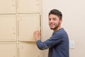 Young handsome man wearing blue sweater smiling and opening metal locker door, rack of lockers stacked Royalty Free Stock Photo