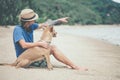 Young handsome man wearing blue t-shirt, hat and sunglasses, sitting on the beach with the dog Royalty Free Stock Photo