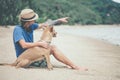 Young handsome man wearing blue t-shirt, hat and sunglasses, sitting on the beach with the dog in Thailand Royalty Free Stock Photo