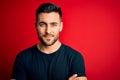 Young handsome man wearing casual black t-shirt standing over isolated red background happy face smiling with crossed arms looking Royalty Free Stock Photo