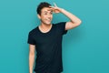 Young handsome man wearing casual black t shirt very happy and smiling looking far away with hand over head Royalty Free Stock Photo