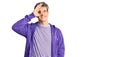 Young handsome man wearing casual purple sweatshirt doing ok gesture with hand smiling, eye looking through fingers with happy Royalty Free Stock Photo
