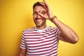 Young handsome man wearing casual red striped t-shirt over yellow isolated background doing ok gesture with hand smiling, eye Royalty Free Stock Photo