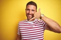 Young handsome man wearing casual red striped t-shirt over yellow isolated background smiling doing phone gesture with hand and Royalty Free Stock Photo