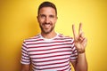 Young handsome man wearing casual red striped t-shirt over yellow isolated background smiling with happy face winking at the Royalty Free Stock Photo
