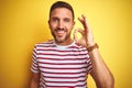 Young handsome man wearing casual red striped t-shirt over yellow isolated background smiling positive doing ok sign with hand and Royalty Free Stock Photo