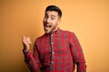 Young handsome man wearing casual shirt standing over isolated yellow background smiling with happy face looking and pointing to Royalty Free Stock Photo