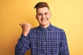 Young handsome man wearing casual shirt standing over isolated yellow background smiling with happy face looking and pointing to Royalty Free Stock Photo