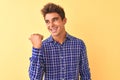 Young handsome man wearing casual shirt standing over isolated yellow background smiling with happy face looking and pointing to Royalty Free Stock Photo