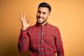 Young handsome man wearing casual shirt standing over isolated yellow background smiling positive doing ok sign with hand and Royalty Free Stock Photo