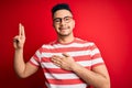 Young handsome man wearing casual striped t-shirt and glasses over isolated red background smiling swearing with hand on chest and Royalty Free Stock Photo