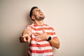 Young handsome man wearing casual striped t-shirt standing over isolated white background laughing at you, pointing finger to the Royalty Free Stock Photo