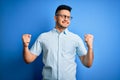 Young handsome man wearing casual summer shirt and glasses over isolated blue background very happy and excited doing winner Royalty Free Stock Photo