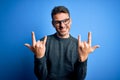 Young handsome man wearing casual sweater and glasses standing over blue background shouting with crazy expression doing rock Royalty Free Stock Photo