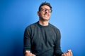 Young handsome man wearing casual sweater and glasses standing over blue background very happy and excited doing winner gesture Royalty Free Stock Photo