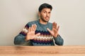 Young handsome man wearing casual sweater sitting on the table disgusted expression, displeased and fearful doing disgust face Royalty Free Stock Photo