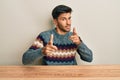 Young handsome man wearing casual sweater sitting on the table pointing fingers to camera with happy and funny face Royalty Free Stock Photo