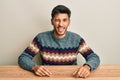 Young handsome man wearing casual sweater sitting on the table winking looking at the camera with sexy expression, cheerful and Royalty Free Stock Photo