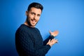 Young handsome man wearing casual sweater standing over isolated blue background Inviting to enter smiling natural with open hand Royalty Free Stock Photo