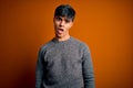 Young handsome man wearing casual sweater standing over isolated orange background In shock face, looking skeptical and sarcastic, Royalty Free Stock Photo