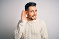 Young handsome man wearing casual sweater standing over isolated white background smiling with hand over ear listening an hearing Royalty Free Stock Photo