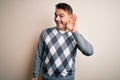 Young handsome man wearing casual sweater standing over isolated white background smiling with hand over ear listening an hearing Royalty Free Stock Photo