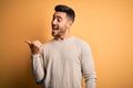 Young handsome man wearing casual sweater standing over isolated yellow background smiling with happy face looking and pointing to Royalty Free Stock Photo