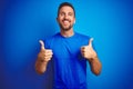 Young handsome man wearing casual t-shirt over blue  background success sign doing positive gesture with hand, thumbs up Royalty Free Stock Photo