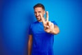 Young handsome man wearing casual t-shirt over blue isolated background smiling looking to the camera showing fingers doing Royalty Free Stock Photo