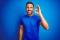 Young handsome man wearing casual t-shirt over blue isolated background smiling positive doing ok sign with hand and fingers Royalty Free Stock Photo