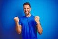 Young handsome man wearing casual t-shirt over blue isolated background very happy and excited doing winner gesture with arms Royalty Free Stock Photo