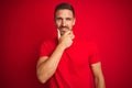 Young handsome man wearing casual t-shirt over red isolated background looking confident at the camera smiling with crossed arms Royalty Free Stock Photo