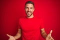 Young handsome man wearing casual t-shirt over red isolated background smiling cheerful with open arms as friendly welcome, Royalty Free Stock Photo