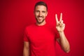 Young handsome man wearing casual t-shirt over red isolated background smiling looking to the camera showing fingers doing victory Royalty Free Stock Photo