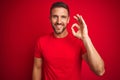 Young handsome man wearing casual t-shirt over red isolated background smiling positive doing ok sign with hand and fingers Royalty Free Stock Photo