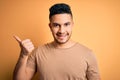 Young handsome man wearing casual t-shirt standing over isolated yellow background smiling with happy face looking and pointing to Royalty Free Stock Photo