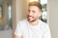 Young handsome man wearing casual white t-shirt at home looking away to side with smile on face, natural expression Royalty Free Stock Photo