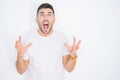 Young handsome man wearing casual white t-shirt over white isolated background crazy and mad shouting and yelling with aggressive Royalty Free Stock Photo