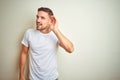 Young handsome man wearing casual white t-shirt over isolated background smiling with hand over ear listening an hearing to rumor Royalty Free Stock Photo