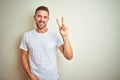 Young handsome man wearing casual white t-shirt over isolated background smiling looking to the camera showing fingers doing Royalty Free Stock Photo