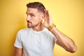 Young handsome man wearing casual white t-shirt over yellow isolated background smiling with hand over ear listening an hearing to Royalty Free Stock Photo