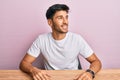 Young handsome man wearing casual white t-shirt sitting on the table looking away to side with smile on face, natural expression Royalty Free Stock Photo