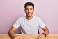 Young handsome man wearing casual white t-shirt sitting on the table looking positive and happy standing and smiling with a Royalty Free Stock Photo