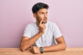 Young handsome man wearing casual white t-shirt sitting on the table serious face thinking about question with hand on chin, Royalty Free Stock Photo