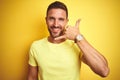 Young handsome man wearing casual yellow t-shirt over yellow isolated background smiling doing phone gesture with hand and fingers Royalty Free Stock Photo
