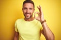 Young handsome man wearing casual yellow t-shirt over yellow isolated background smiling positive doing ok sign with hand and Royalty Free Stock Photo