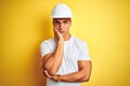 Young handsome man wearing construction helmet over yellow isolated background thinking looking tired and bored with depression