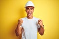 Young handsome man wearing construction helmet over yellow isolated background very happy and excited doing winner gesture with